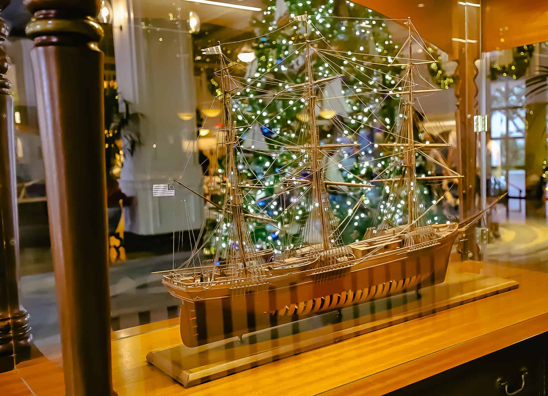 A model ship in a glass case with the lights of the Christmas tree shining behind it. 