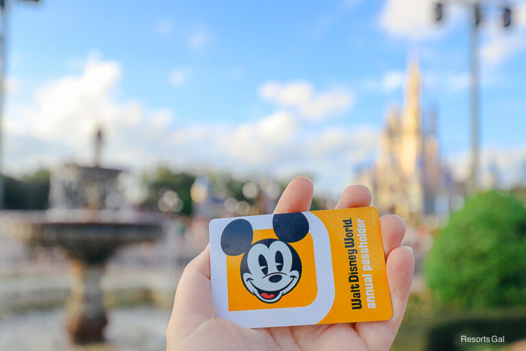 a hand holding an annual pass in front of Cinderella Castle