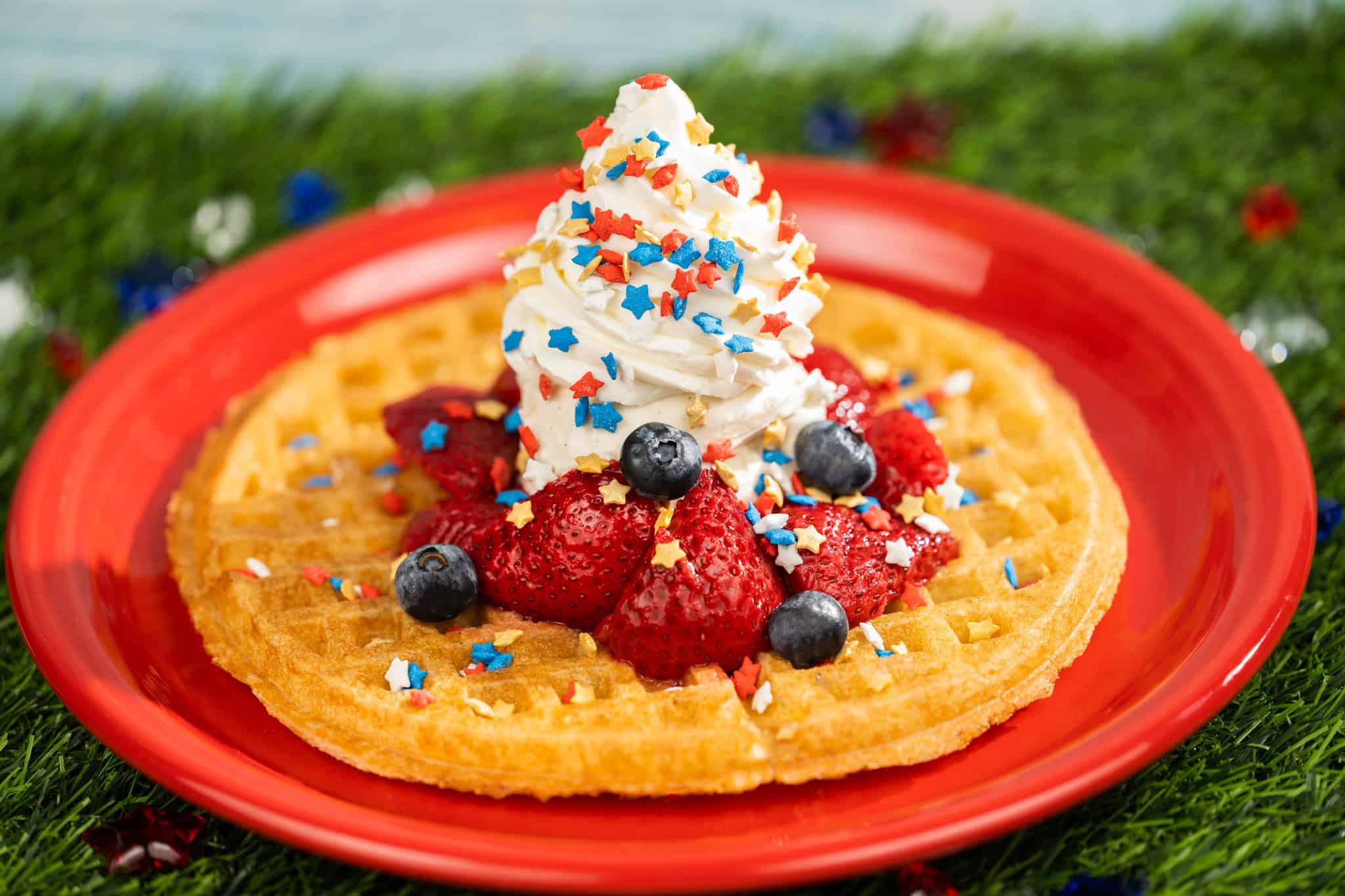a waffle topped with berries, whip cream, and confetti stars