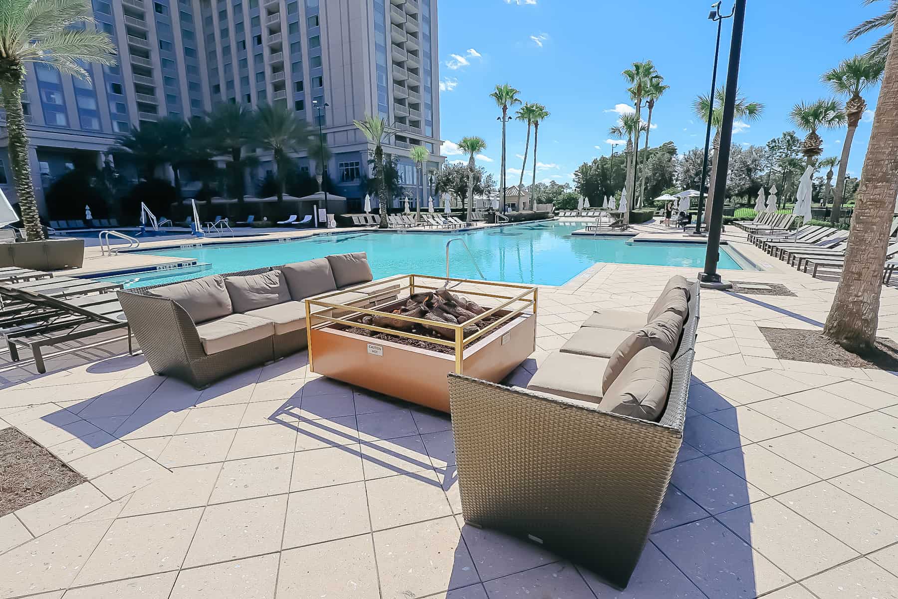 two outdoor sofas sitting on each side of a fire pit near the pool 