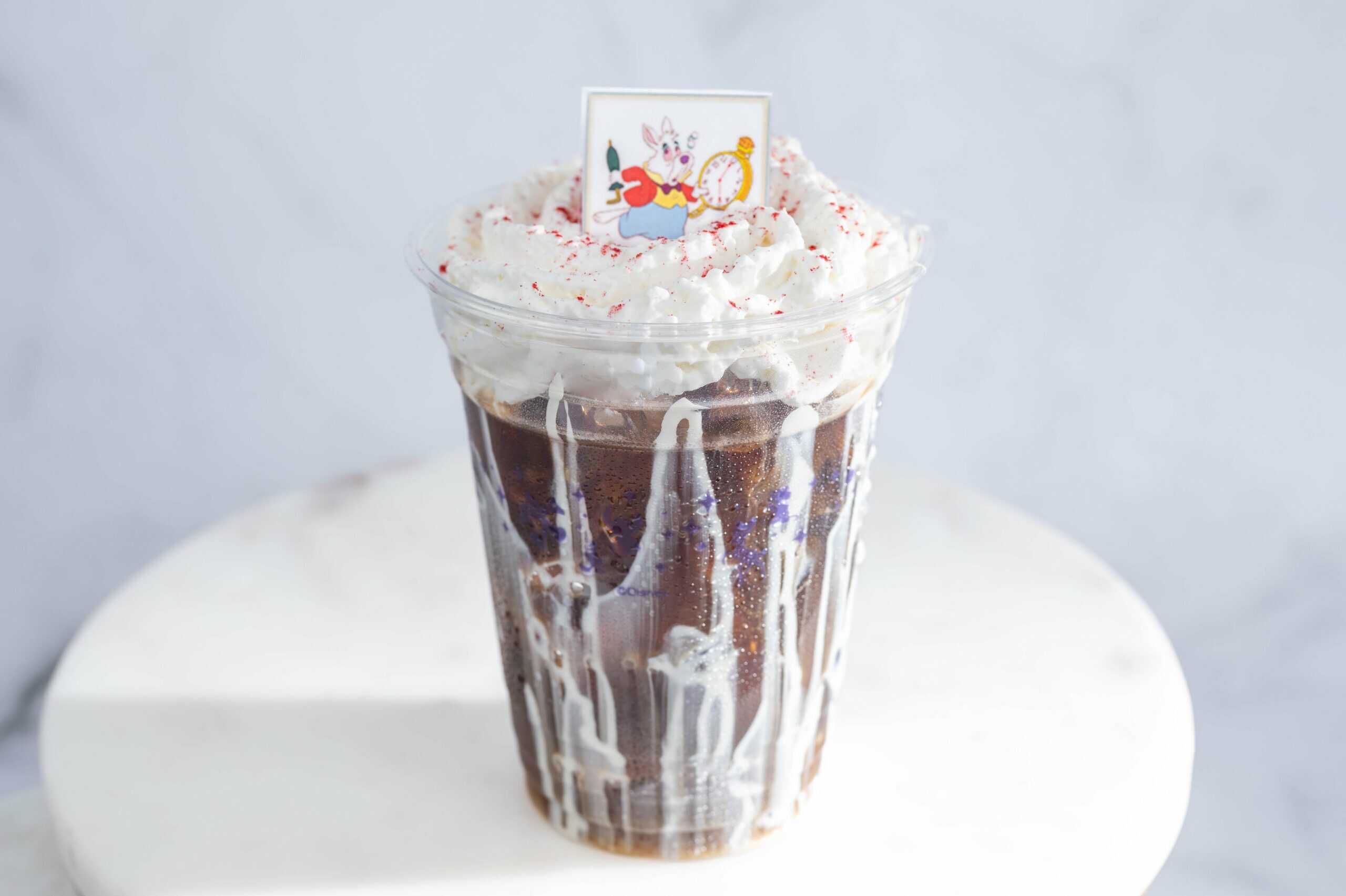 a cold brew coffee topped with a white square featuring the White Rabbit from Alice in Wonderland
