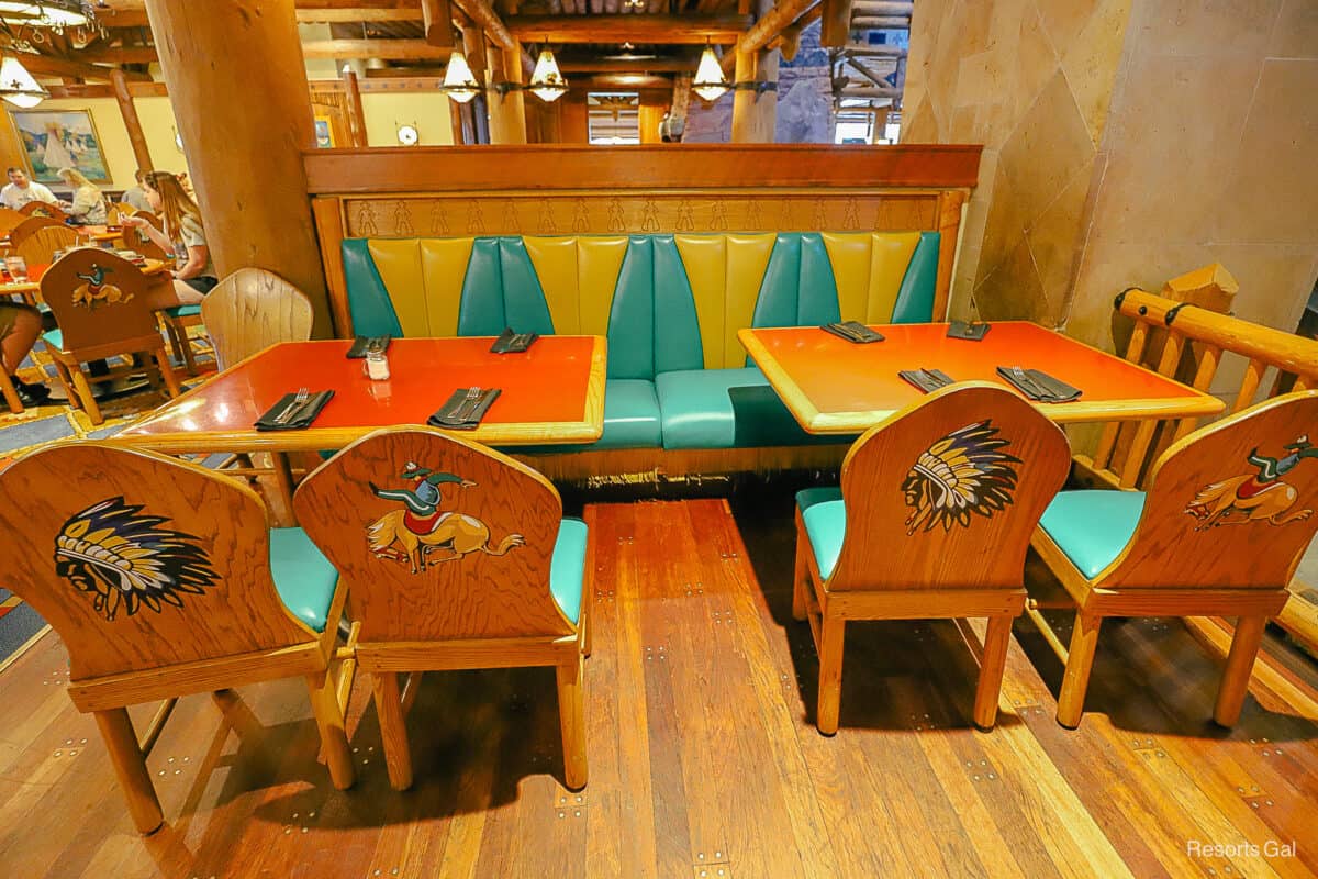 a table and chairs set up inside the restaurant. The chairs have Indians and cowboys painted on the back. 